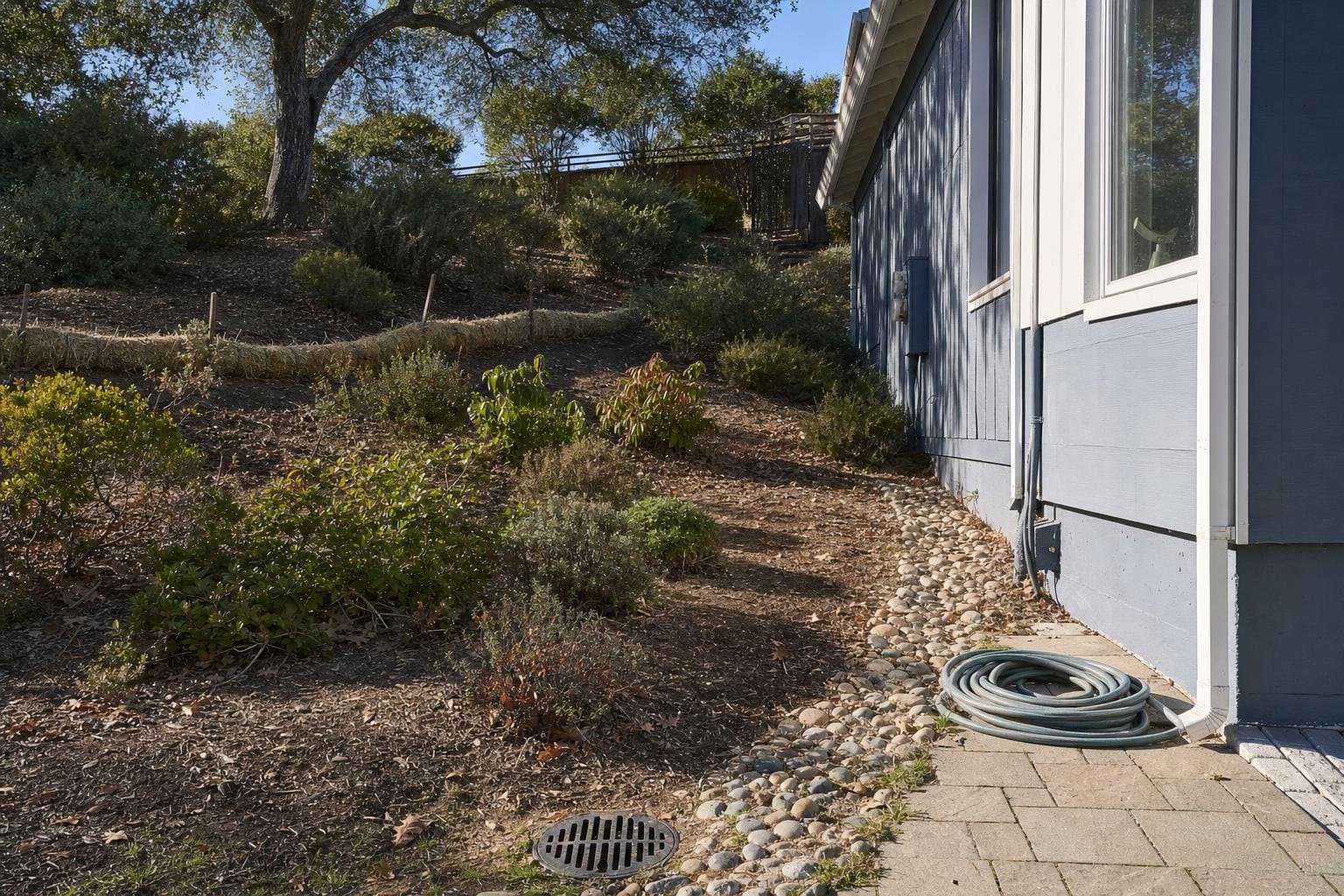 Preparing a yard for rainy season in Santa Cruz with a gravel swale, a clear area drain, and a straw wattle on the slope